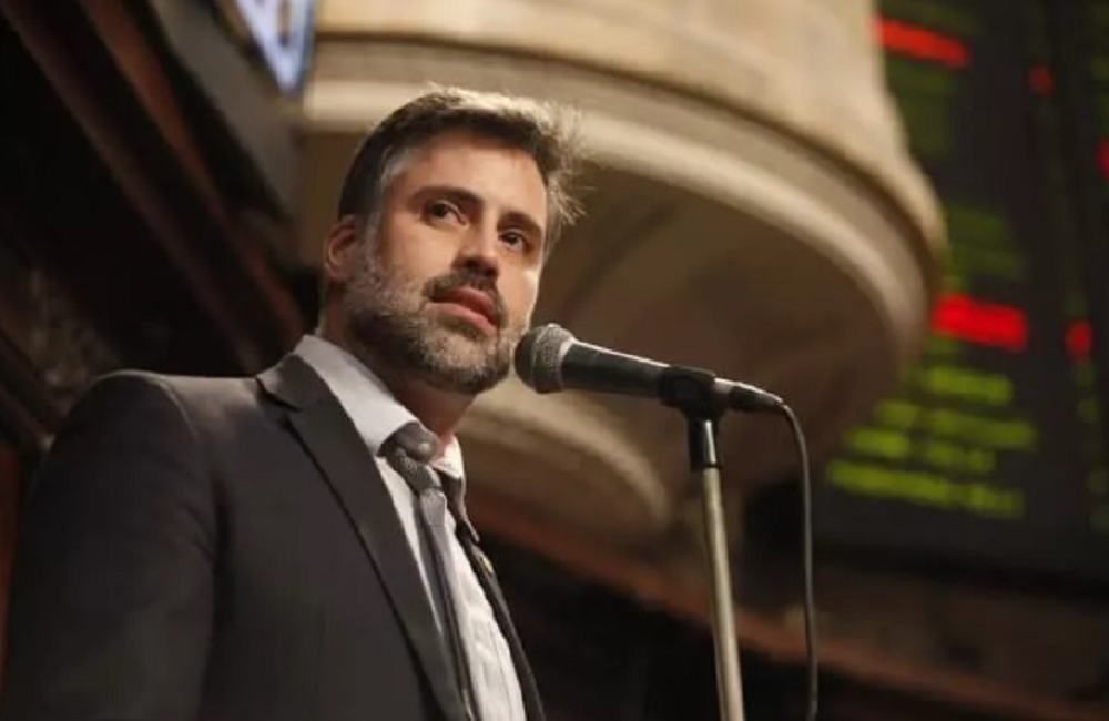 Alexandre Freitas com expressão séria, de terno e gravata, perto de microfone, sem olhar para a câmera