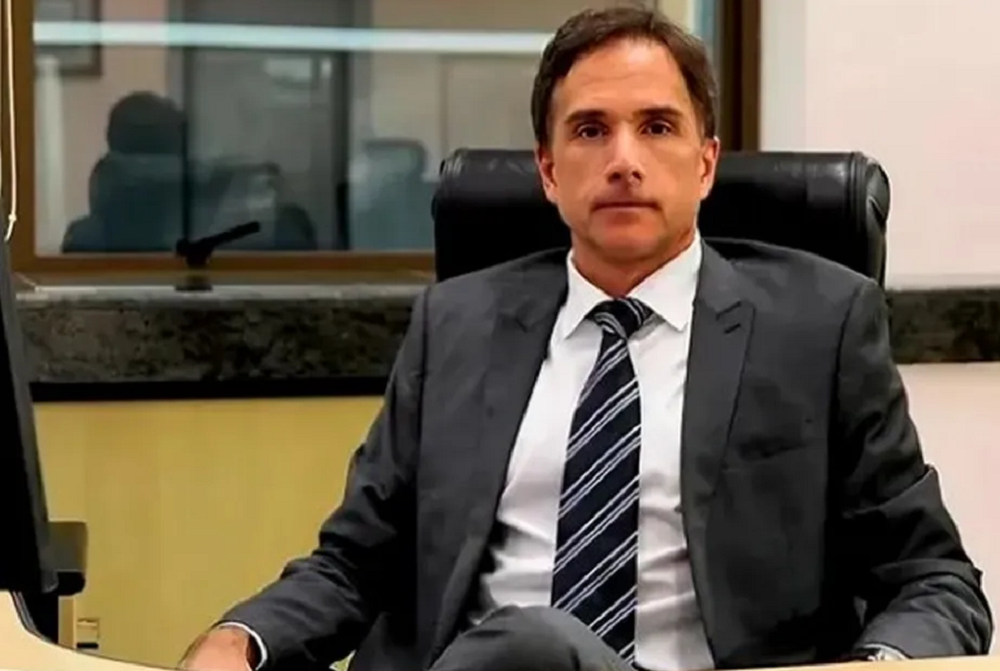 Eduardo Appio sério, posando para foto sentado, de terno e gravata