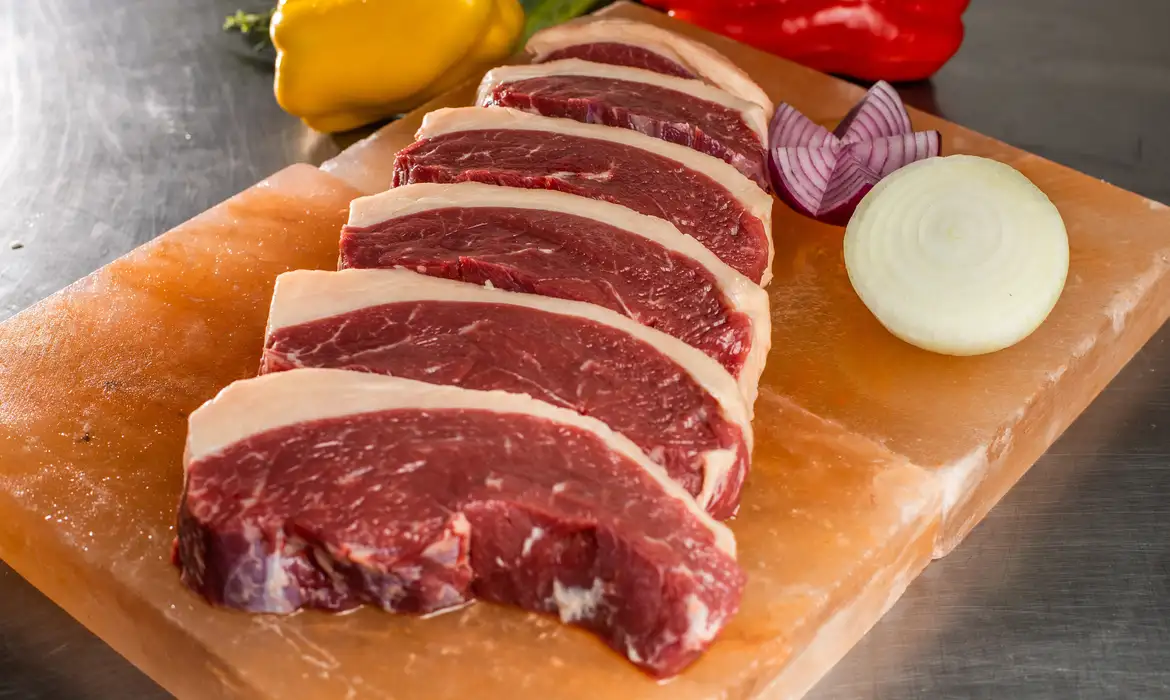 Bifes de carne vermelha em tábua de madeira, com pedaços de cebola