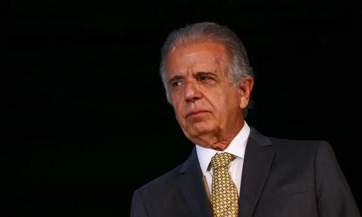 Múcio de terno e gravata, com expressão séria, sem olhar pra câmera