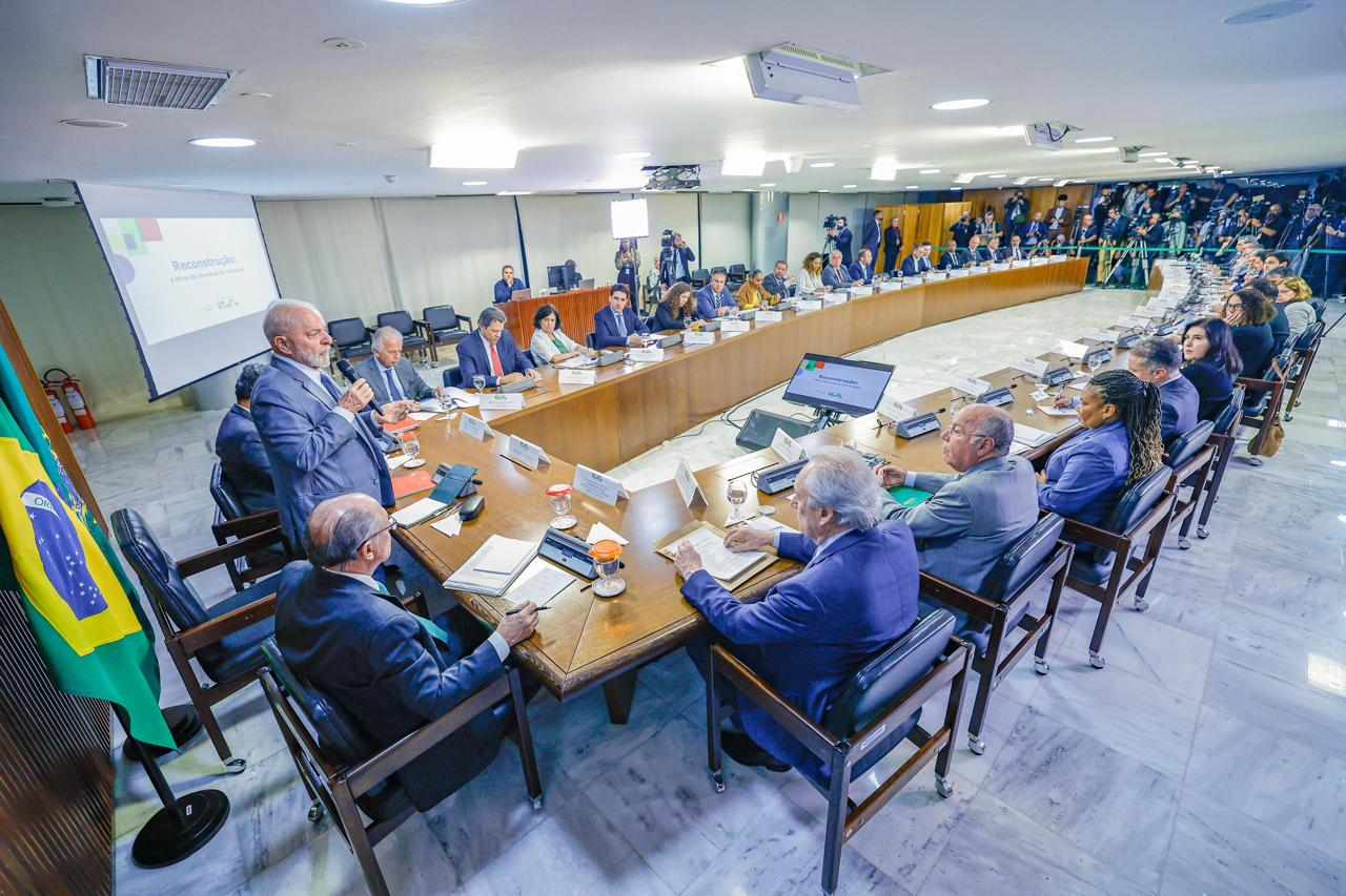 Lula em pé, falando em microfone, cercado de ministros