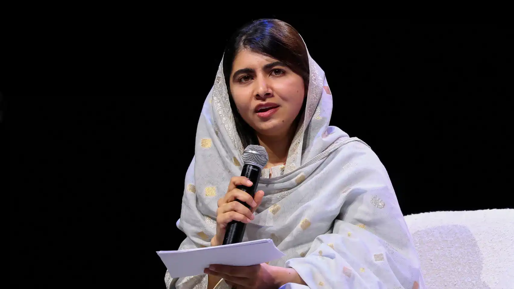 Malala Yousafzai falando em microfone e segurando papel