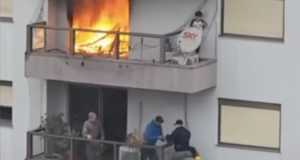 Homens em andar inferior cortando tela e menino acima, em varanda com fogo ao lado
