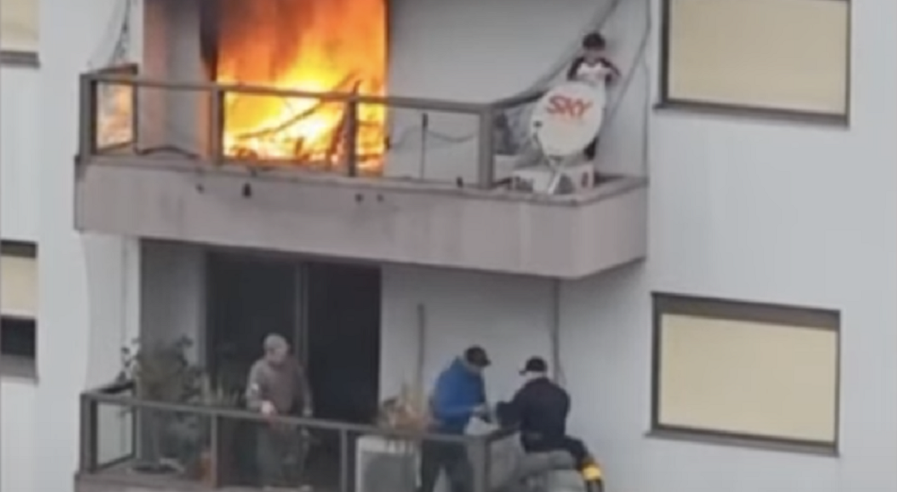 Homens em andar inferior cortando tela e menino acima, em varanda com fogo ao lado