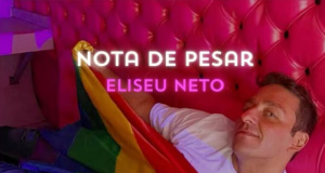 Eliseu Neto em local cor de rosa, de camiseta branca, segurando bandeira