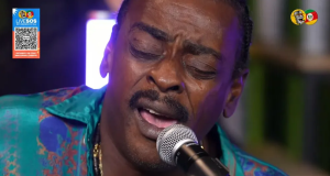 Seu Jorge de roupa estampada e olhos fechados, cantando em microfone, em close
