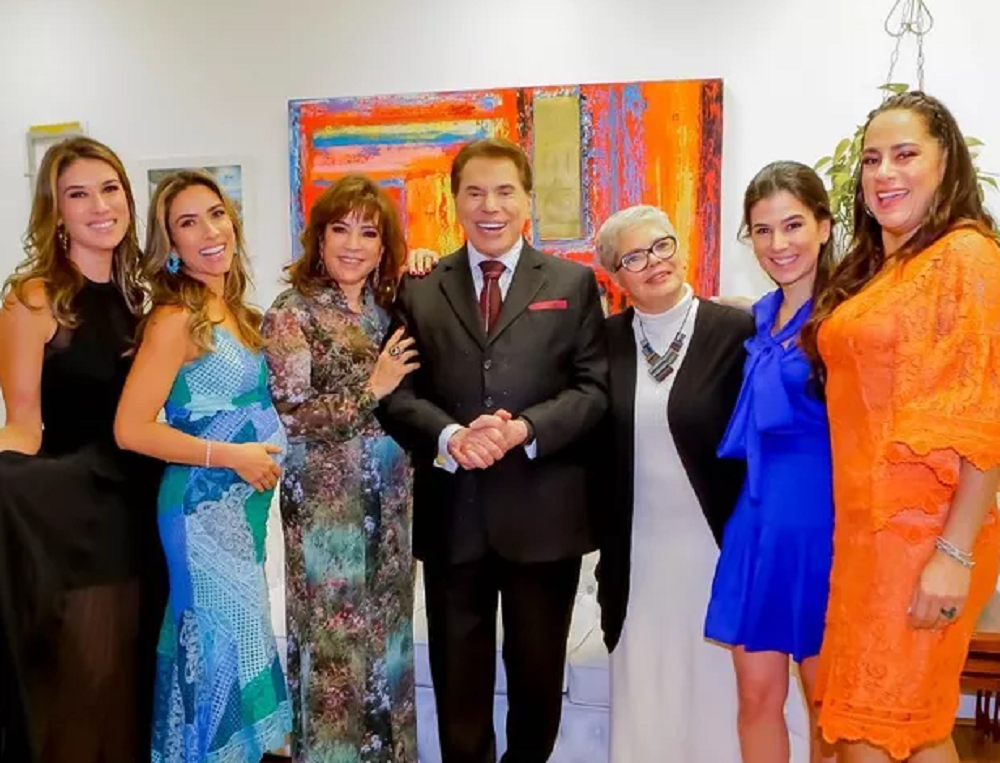 Silvio Santos em foto sorrindo com as filhas e a esposa, todos em pé, lado a lado