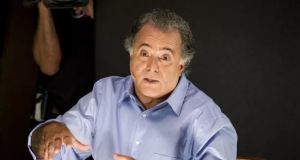 Tony Ramos com expressão séria e roupa azul, falando e gesticulando