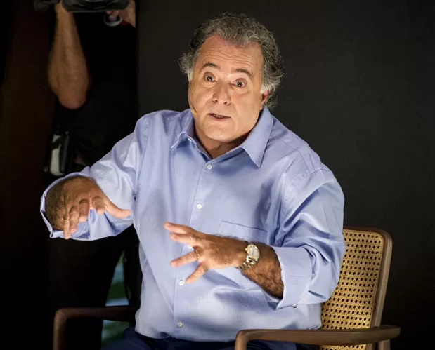 Tony Ramos com expressão séria e roupa azul, falando e gesticulando