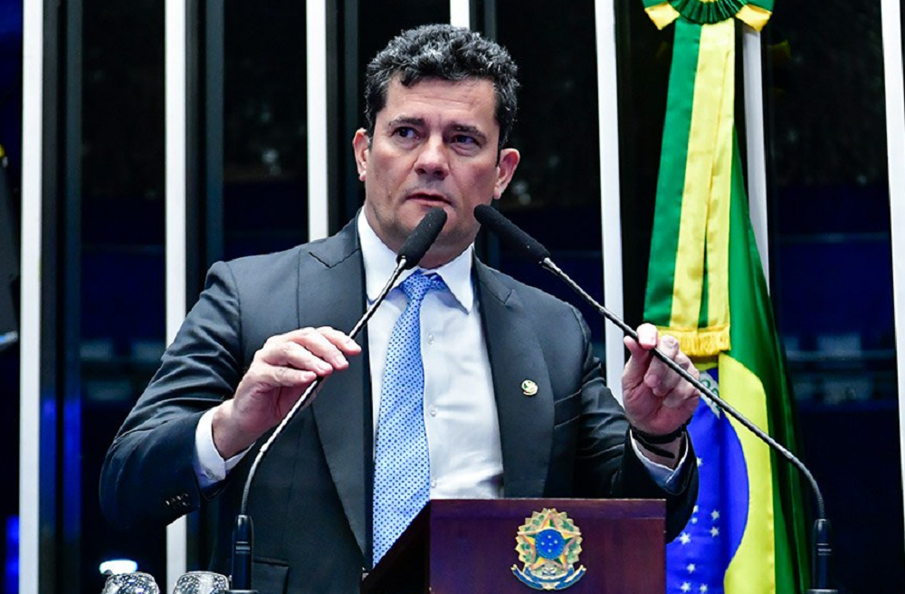 Sergio Moro de terno e gravata, falando em microfones com expressão séria