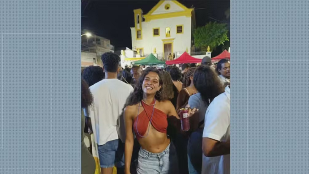 Alma Bohadana posando para foto de short jeans e cropped, sorrindo, na frente de multidão e igreja