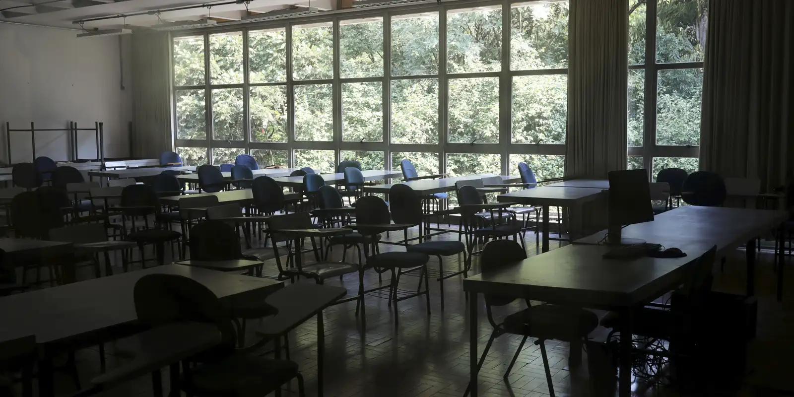 Sala de aula vazia, só com mesas e cadeiras, de dia