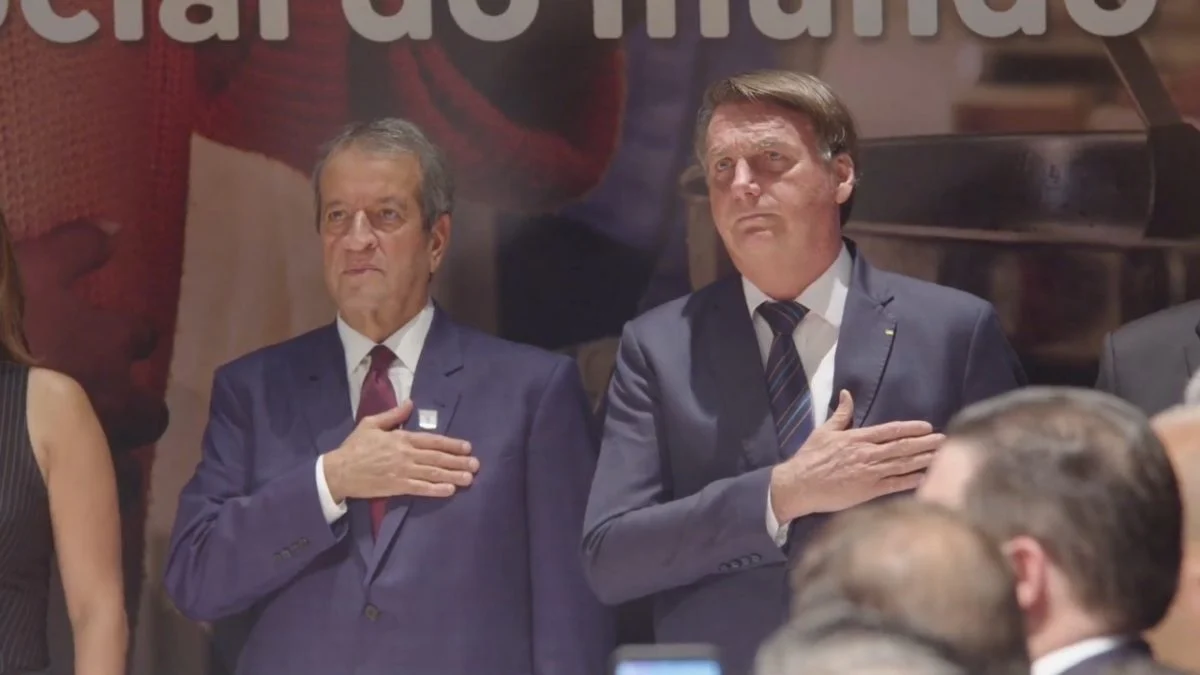 Valdemar Costa Neto e Jair Bolsonaro sérios, em pé, lado a lado, com a mão no peito