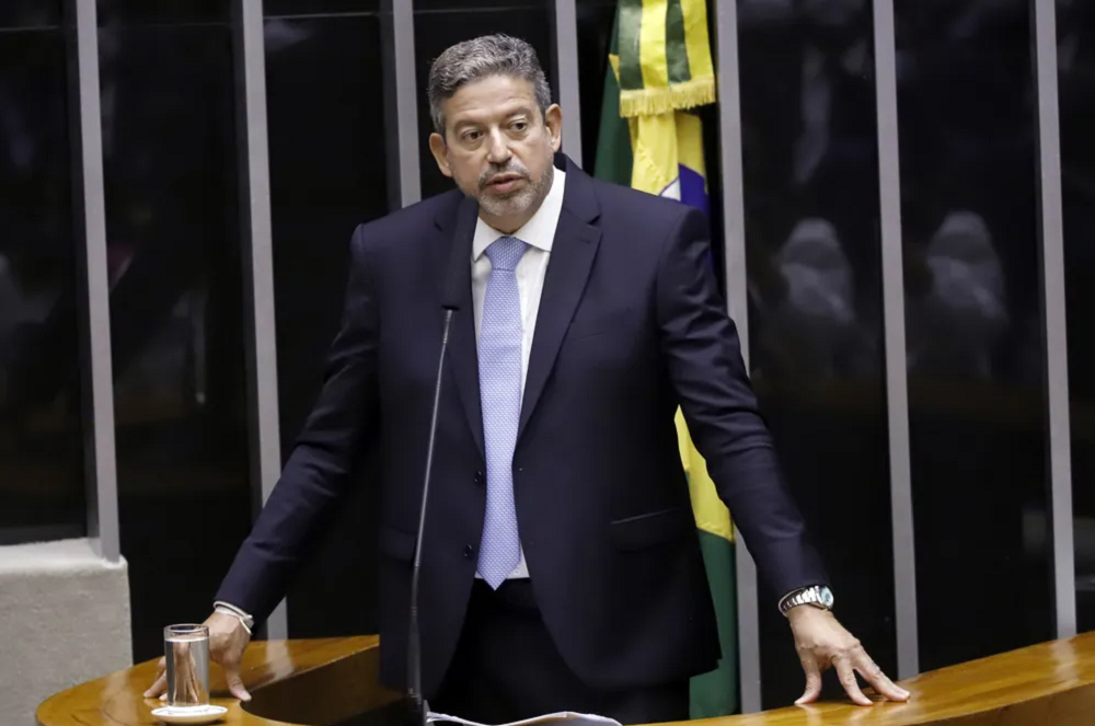 Arthur Lira falando e olhando para o lado, com expressão séria, em pé