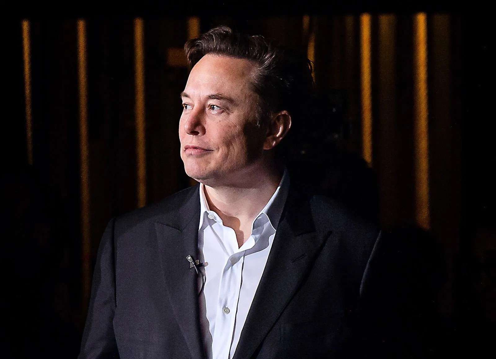 Elon Musk sério, olhando para o lado, de roupa social