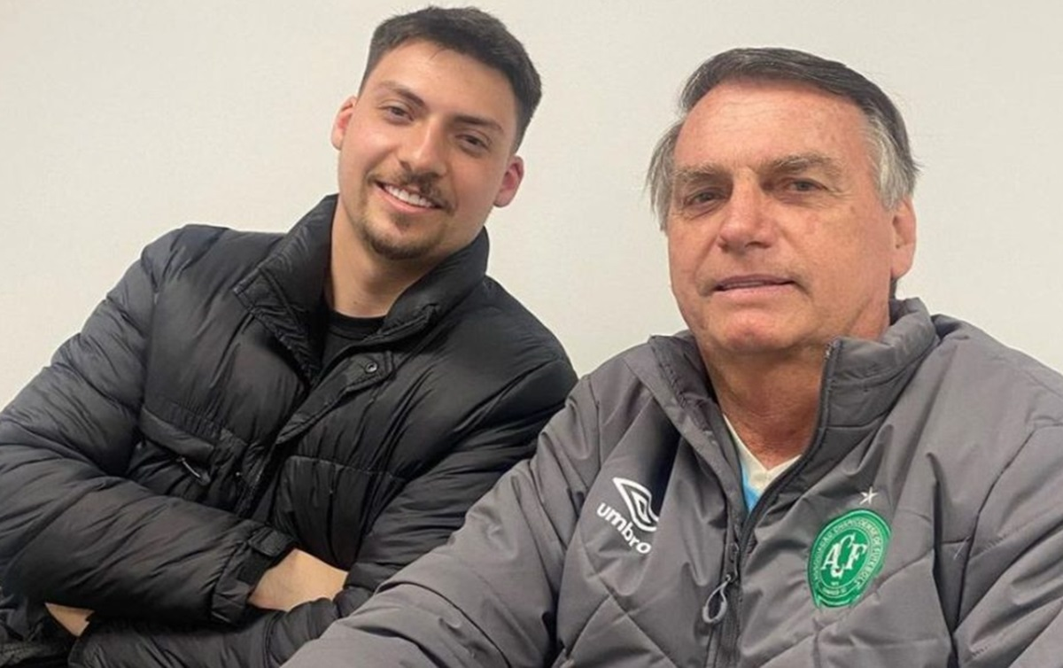 Jair Renan e o pai, o ex-presidente Jair Bolsonaro, posando para foto com sorrisos tímidos e roupa escura