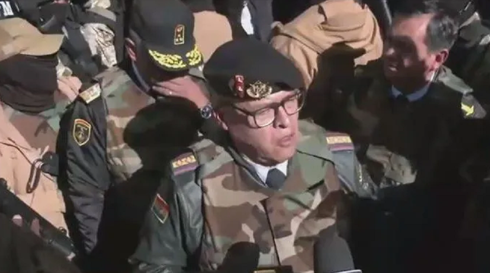 General Juan José Zúñiga cercado de militares, falando com expressão séria e óculos