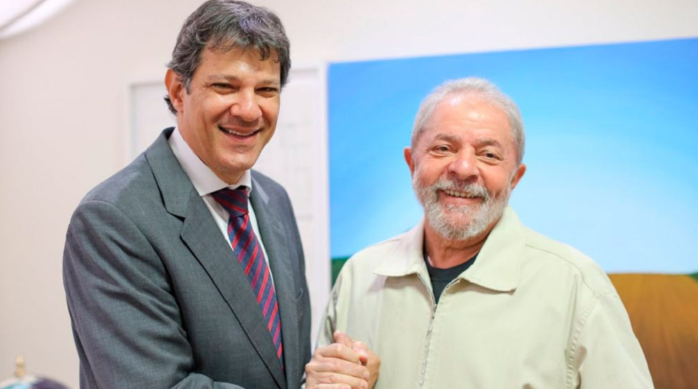 Ministro da Fazenda, Fernando Haddad, e o presidente Lula, de mãos dadas, sorrindo para foto
