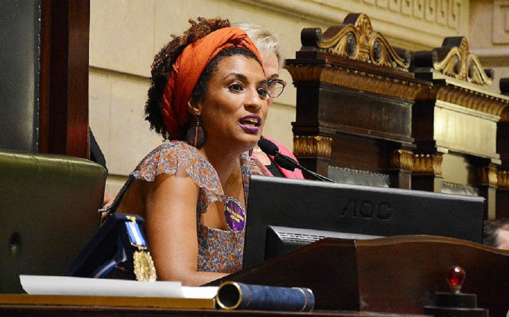 Marielle Franco de roupa estampada e turbante laranja, falando em microfone