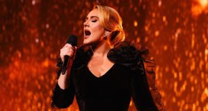 Adele de roupa preta e cabelo preso cantando em microfone