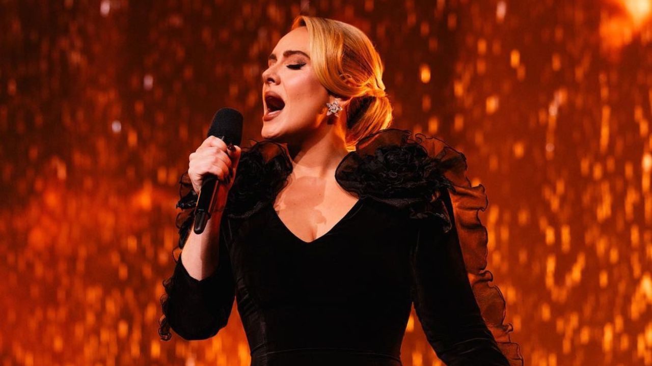 Adele de roupa preta e cabelo preso cantando em microfone