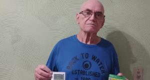 Henrique Manuel Morgado de camiseta azul, sério, segurando documentos de plano de saúde
