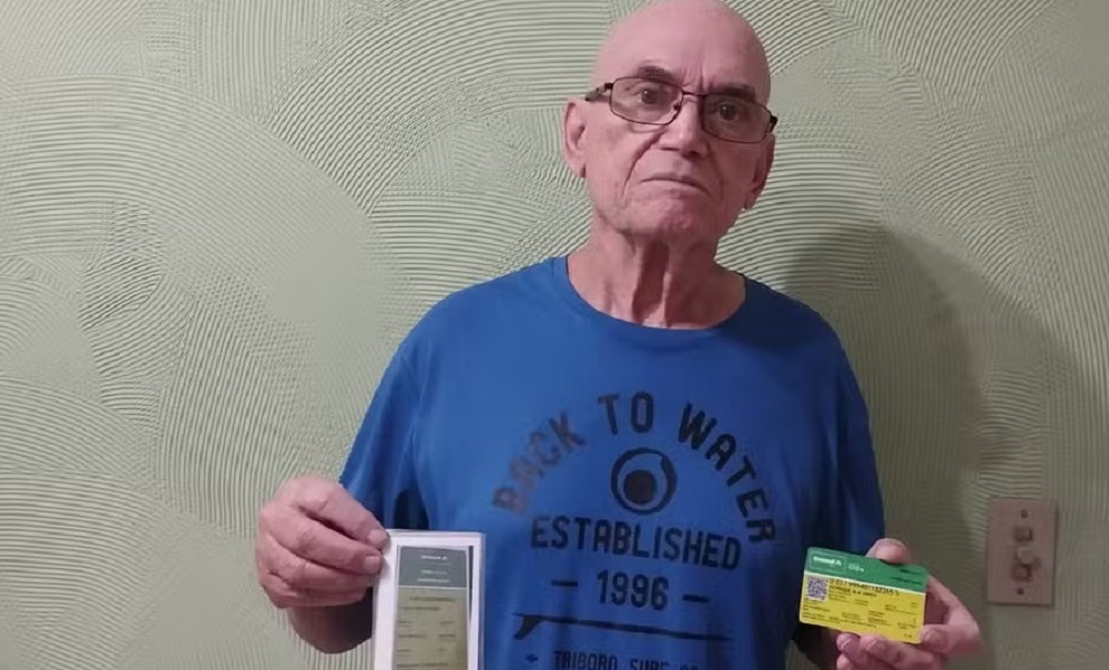 Henrique Manuel Morgado de camiseta azul, sério, segurando documentos de plano de saúde