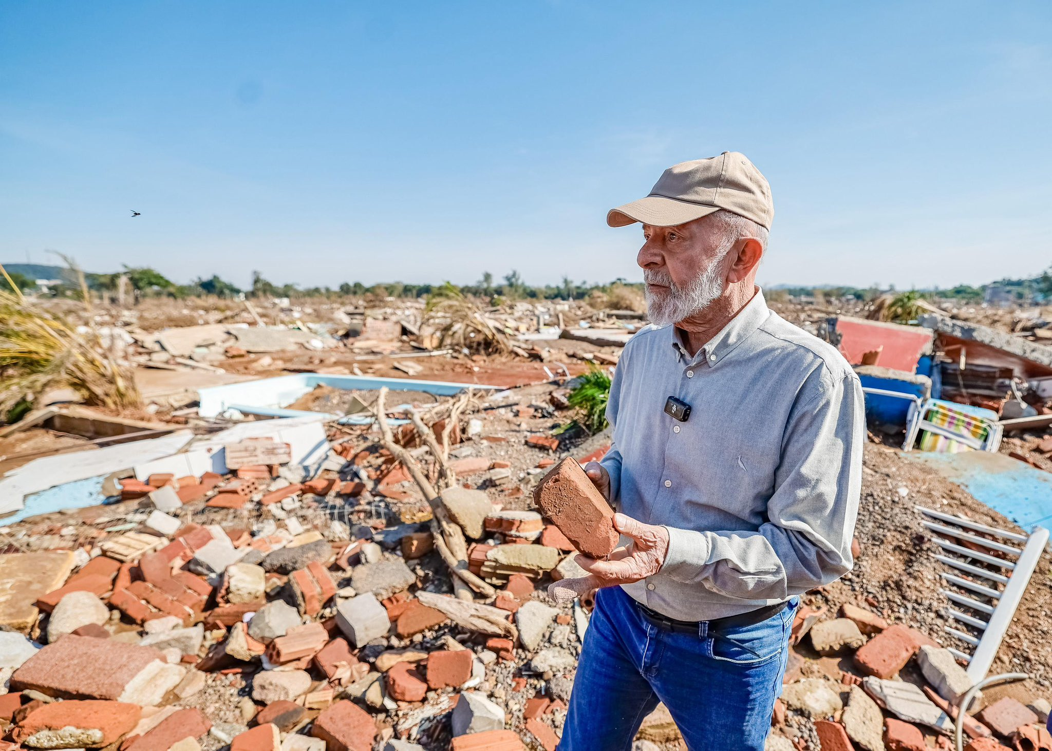 Lula de perfil, andando de boné e roupa social em meio a destroços