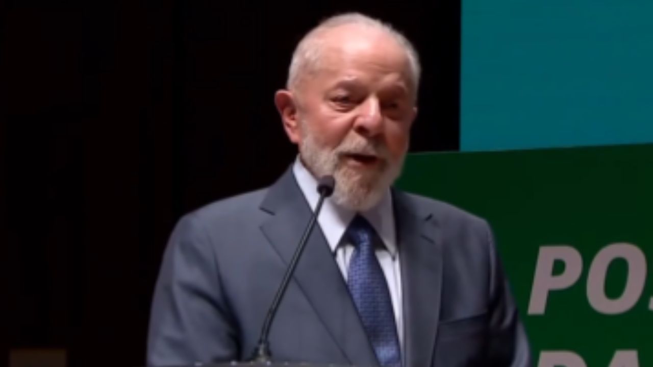 Lula de roupa social cinza, falando em microfone, sério