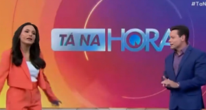 Márcia Dantas e Marcão do Povo lado a lado, em pé, falando e se olhando, no cenário do Tá na Hora