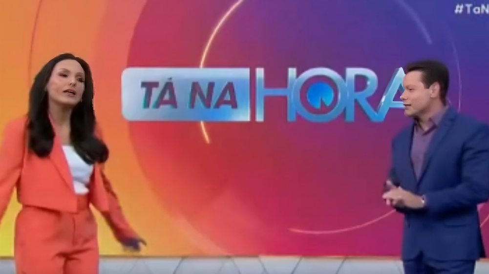 Márcia Dantas e Marcão do Povo lado a lado, em pé, falando e se olhando, no cenário do Tá na Hora