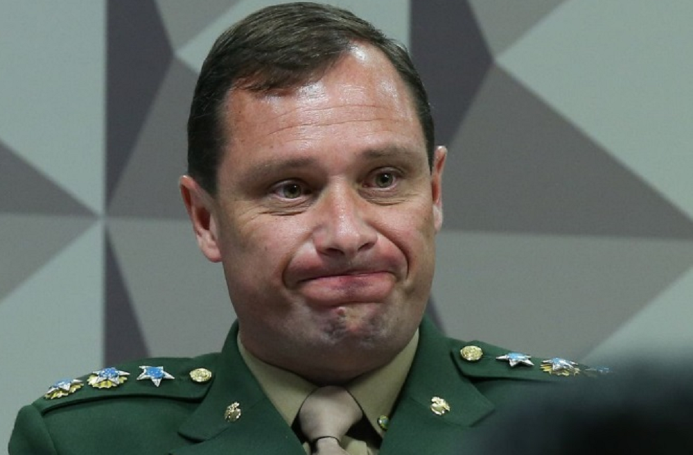 Mauro Cid fardado, com expressão de conformismo, sem olhar para a câmera