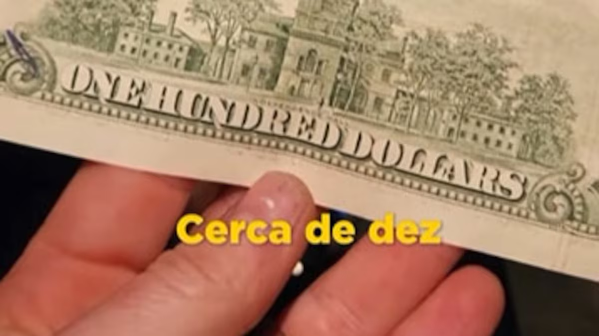 Mão segurando nota de cem dólares com legenda amarela escrito "Cerca de 10"