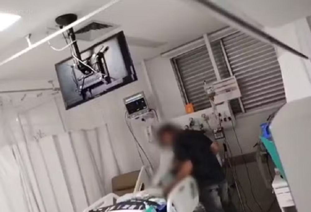 Pai perto de cama da filha em UTI de hospital