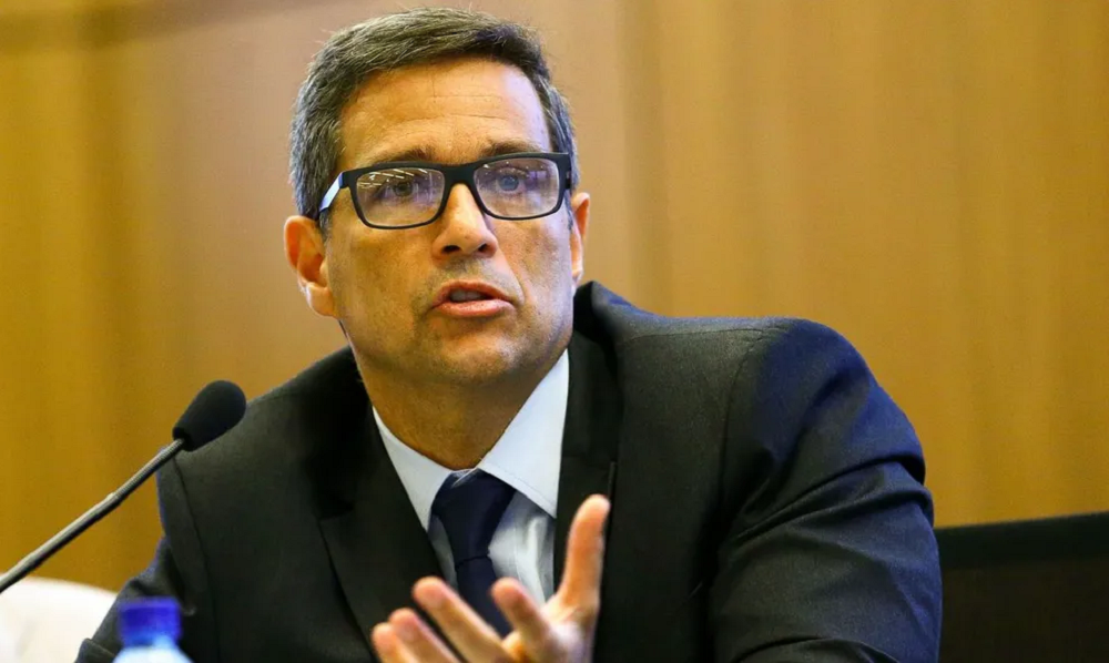 Roberto Campos Neto de óculos, falando com o braço estendido, sério, sem olhar para a câmera
