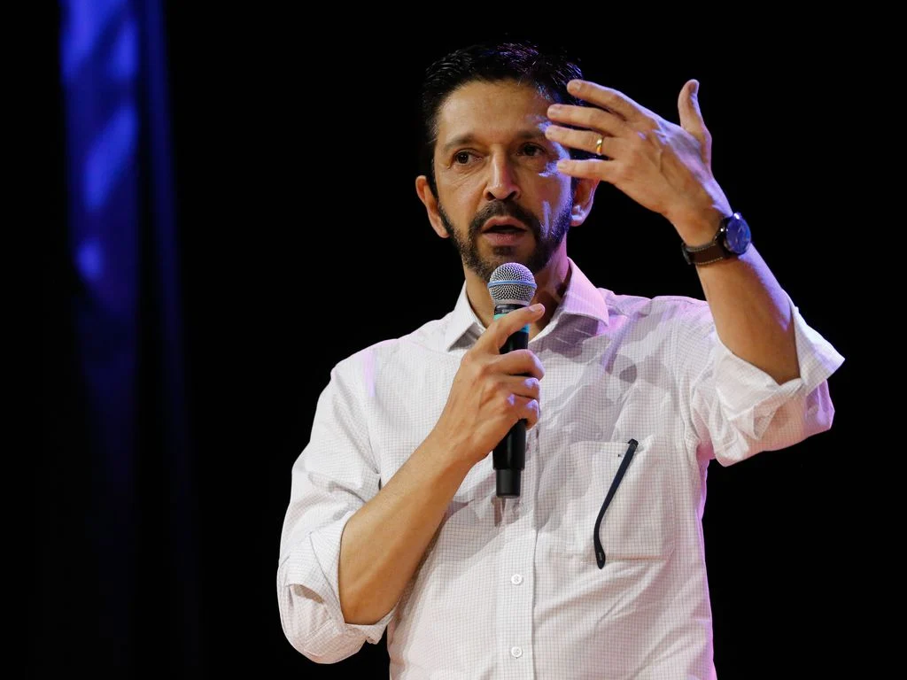 Ricardo Nunes de camisa social branca, falando em microfone e gesticulando