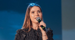 Camila Campos de roupa de poá preta e branca e cabelo solto, cantando em microfone