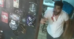 Vanderson Lima em barbearia, em pé, falando e gesticulando