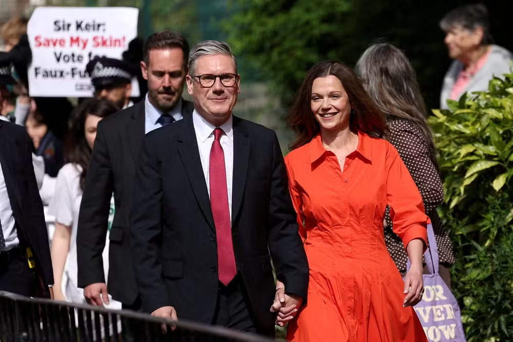 Keir Starmer, líder do Partido Trabalhista, caminhando e sorrindo de mãos dadas com mulher