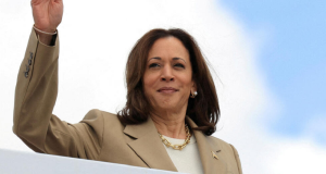 A vice-presidente dos Estados Unidos, Kamala Harris, de roupa bege, com sorriso tímido, acenando, com expressão esperançosa