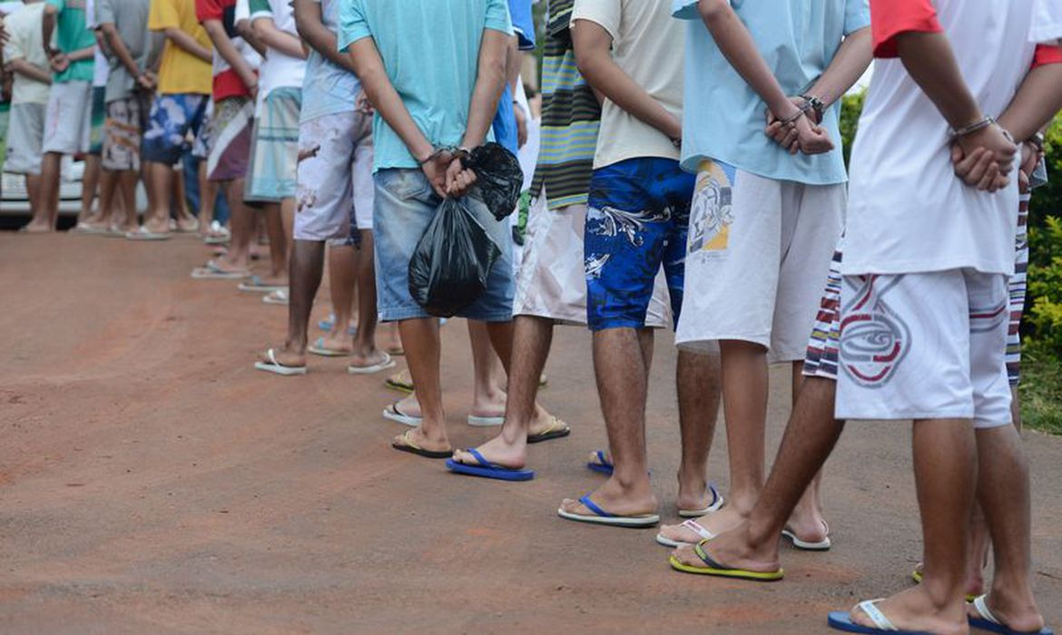 Presos de costas, sem mostrar os rostos, em fila