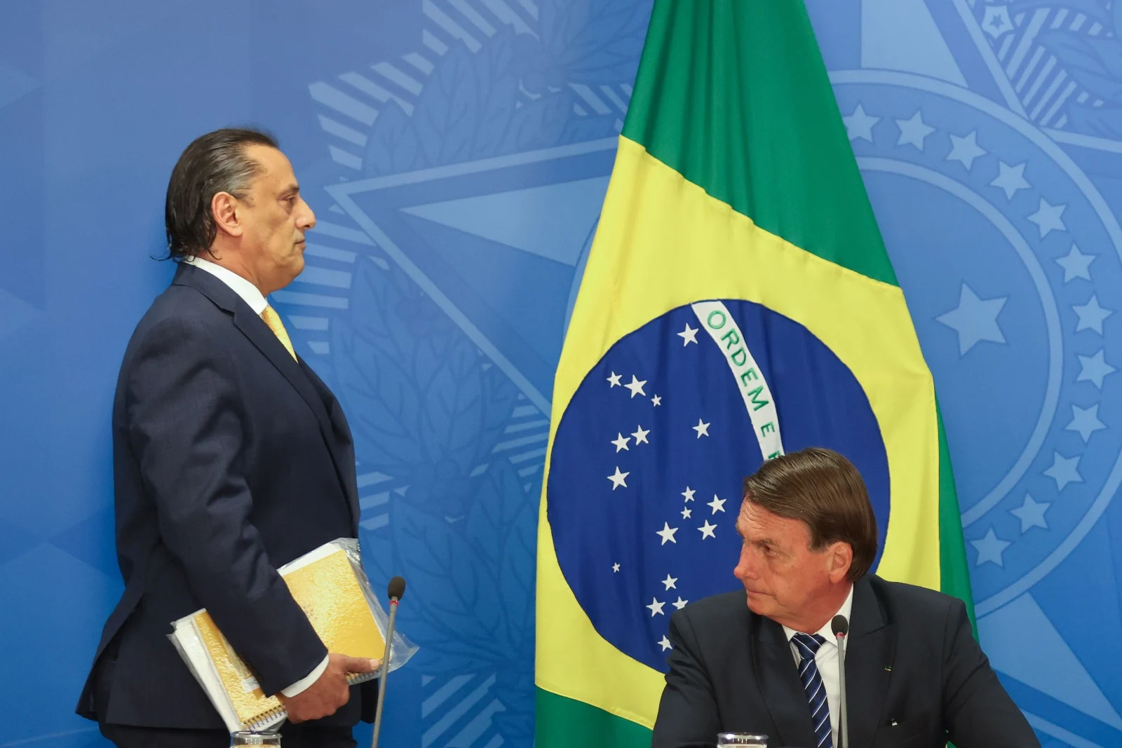 Frederick Wassef em pé, de perfil, e Jair Bolsonaro sentado, olhando para o lado