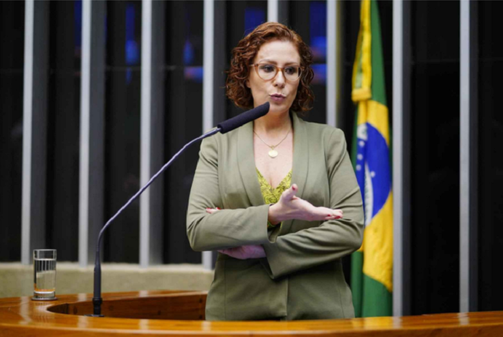 Deputada federal Carla Zambelli (PL-SP) de roupa verde e amarela, em pé, falando em microfone e gesticulando