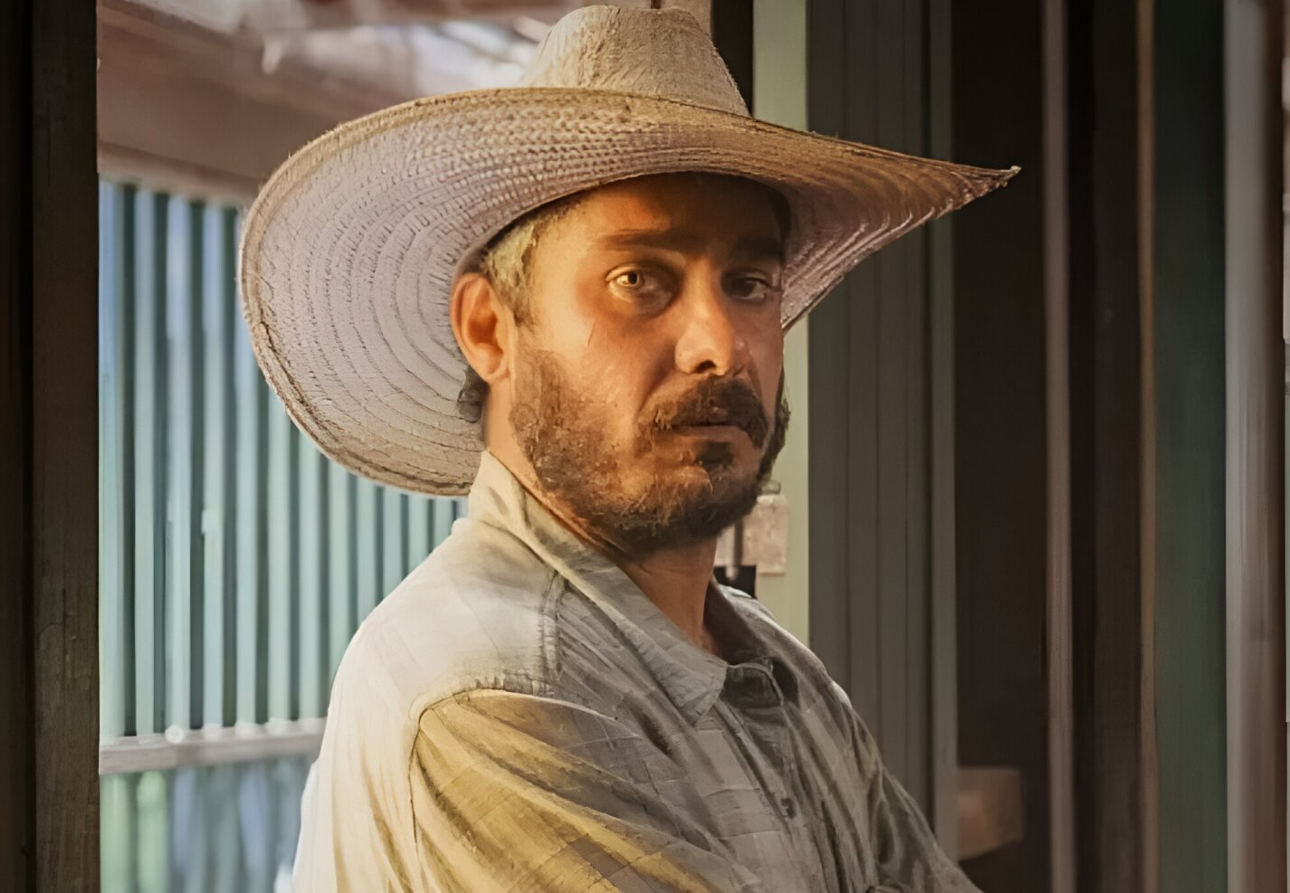 Thommy Schiavo posando sério de chapéu e camisa social clara, olhando para a câmera