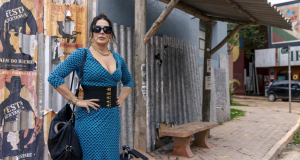 Claudia Raia como a Emmy de Terra e Paixão (2023), de vestido justo azul, cabelo preso e óculos escuros, na rua