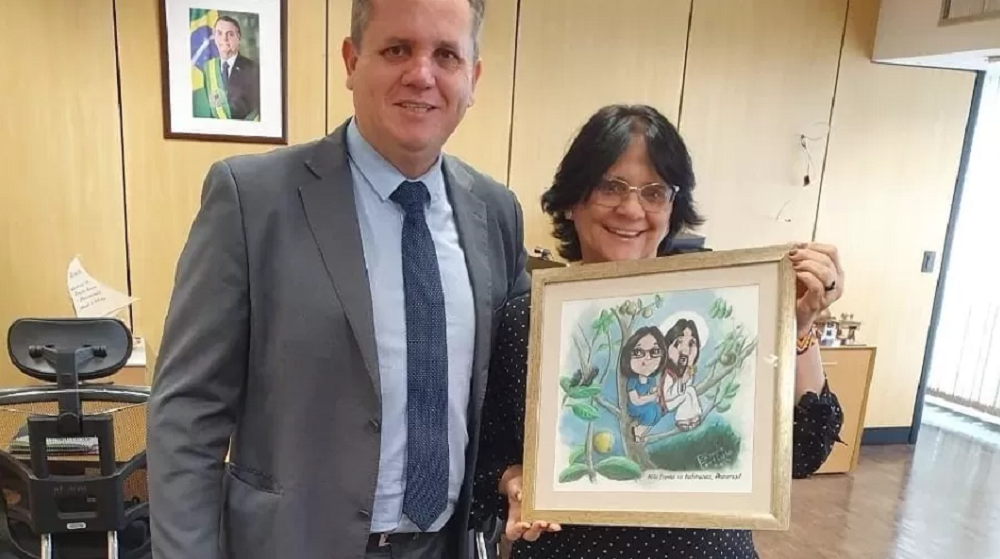 Damares Alves posando com quadro e sorrindo, ao lado de homem