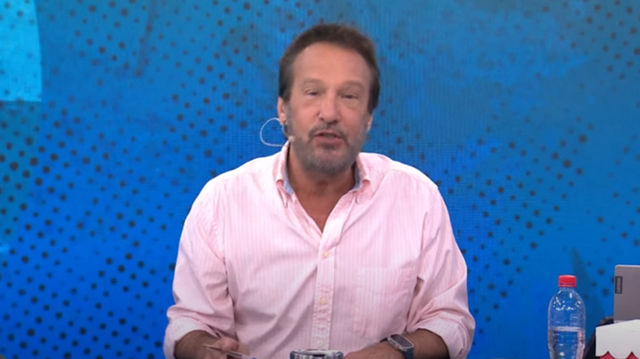 Emílio Surita falando para a câmera, no cenário do programa Pânico, de camisa social cor de rosa