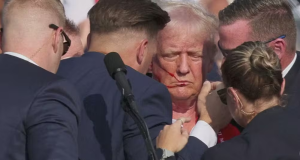 Donald Trump sendo amparado após atentado, de olhos fechados e expressão séria