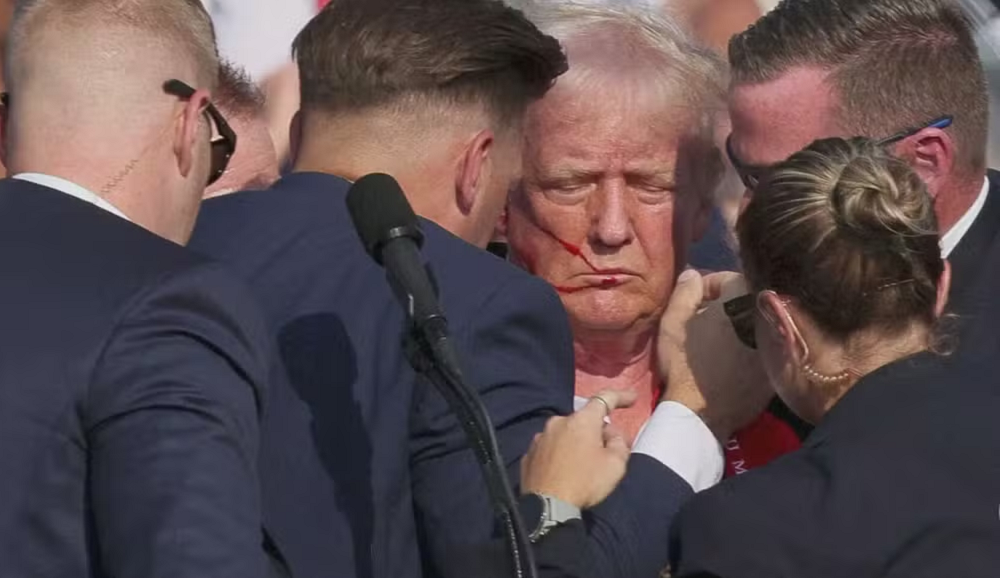 Donald Trump sendo amparado após atentado, de olhos fechados e expressão séria
