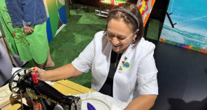 A governadora do Rio Grande do Norte Fátima Bezerra (PT) com máquina de costura, sorrindo, sem olhar pra câmera, de roupa branca
